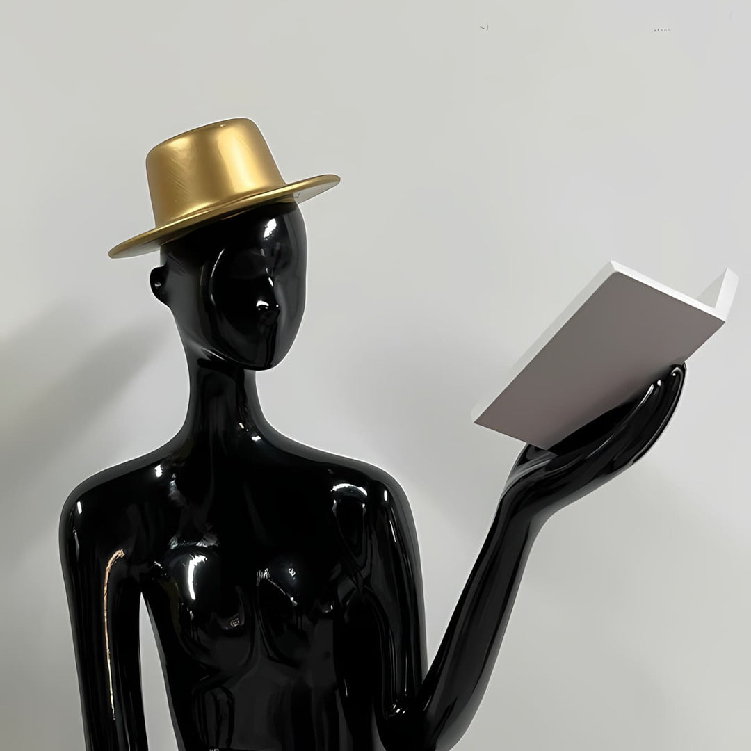 Sculptural floor lamp featuring a black mannequin with a gold hat, holding a book in a modern setting.