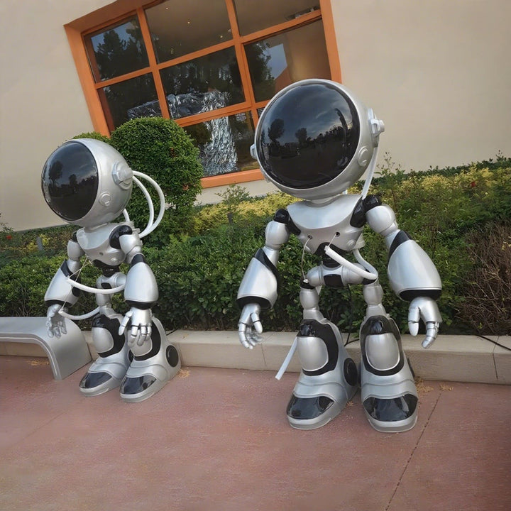 Two futuristic robot sculptures in a garden setting, showcasing a sleek design and shiny metallic finish.