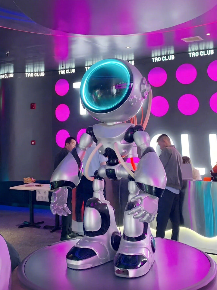 Futuristic robot statue with blue glowing visor in a vibrant nightlife setting at Tao Club.