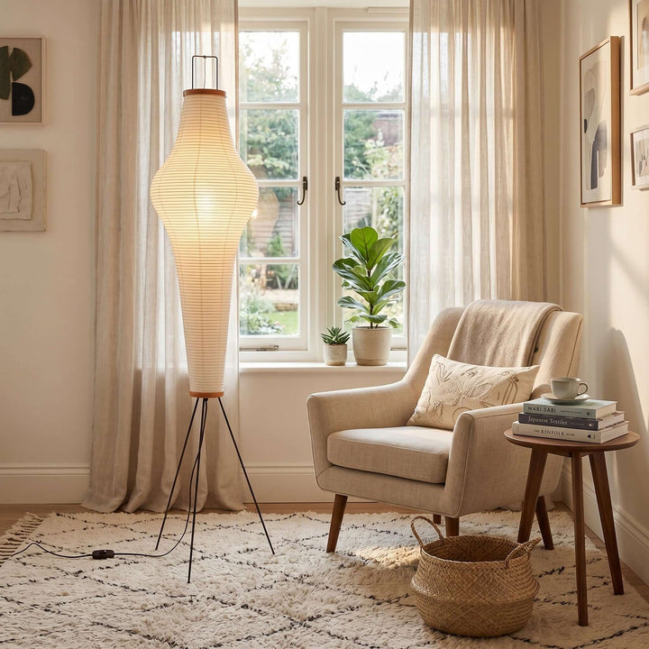 Akari 14A washi paper floor lamp beside a beige armchair and side table in a sunlit reading corner.