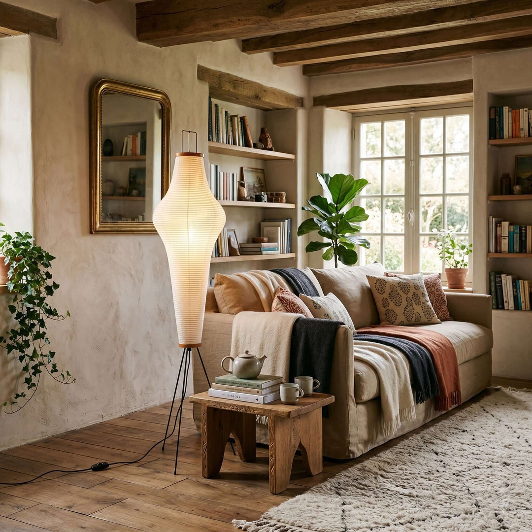 Akari 14A white washi floor lamp beside a neutral sofa in a rustic living room with wood ceiling beams.