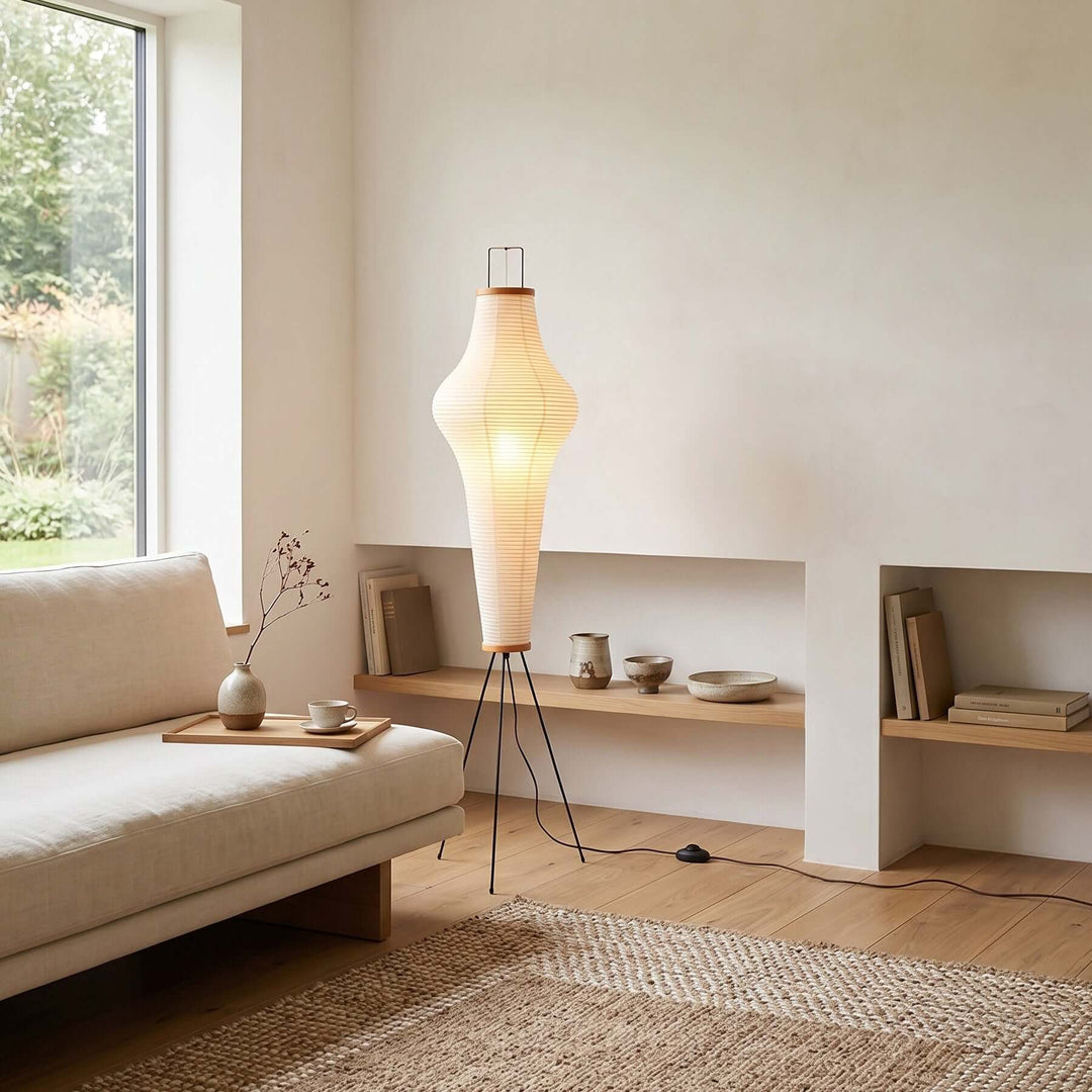 Akari 14A white paper floor lamp beside a low sofa and built-in shelves in a minimalist living room.
