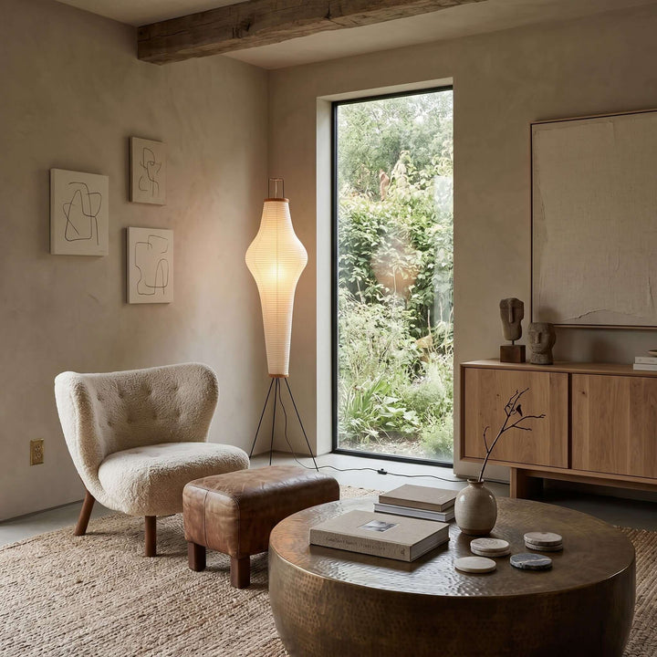 Akari 14A paper floor lamp in a modern living room with a cream chair, leather ottoman, and wood cabinet.