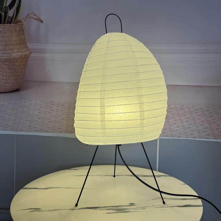 Glowing Akari 1N Table Lamp with black wire legs on a round marble side table