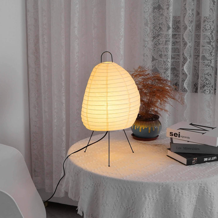Akari 1N Table Lamp casting warm light on a round table with books and a vase