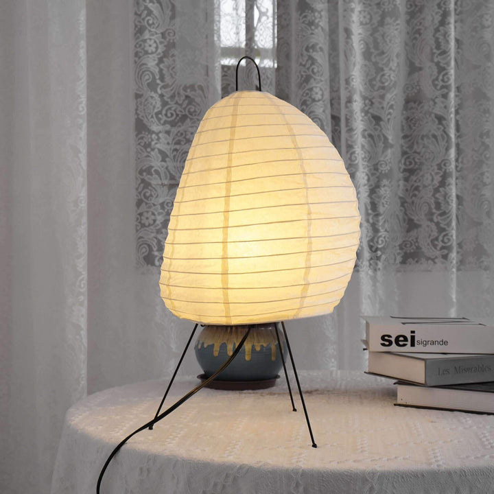 Side view of the Akari 1N rice paper table lamp beside books and decorative pottery