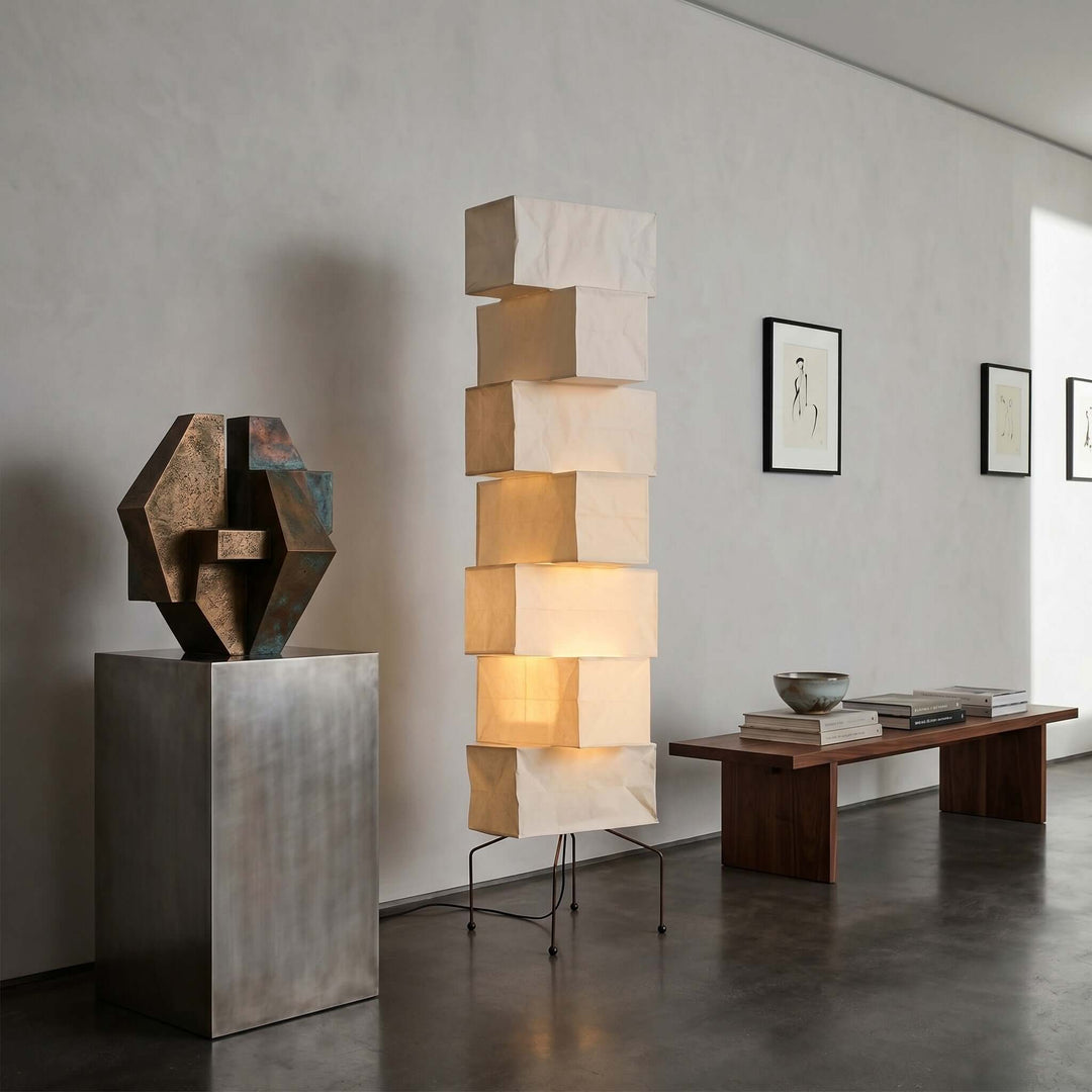 Tall Akari UF4-L10 paper floor lamp displayed with abstract sculpture and a wood bench in a gallery-style interior
