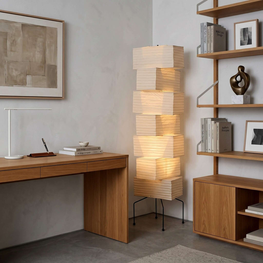 Illuminated Akari rice paper floor lamp between a wood desk and open bookshelf in a modern home office