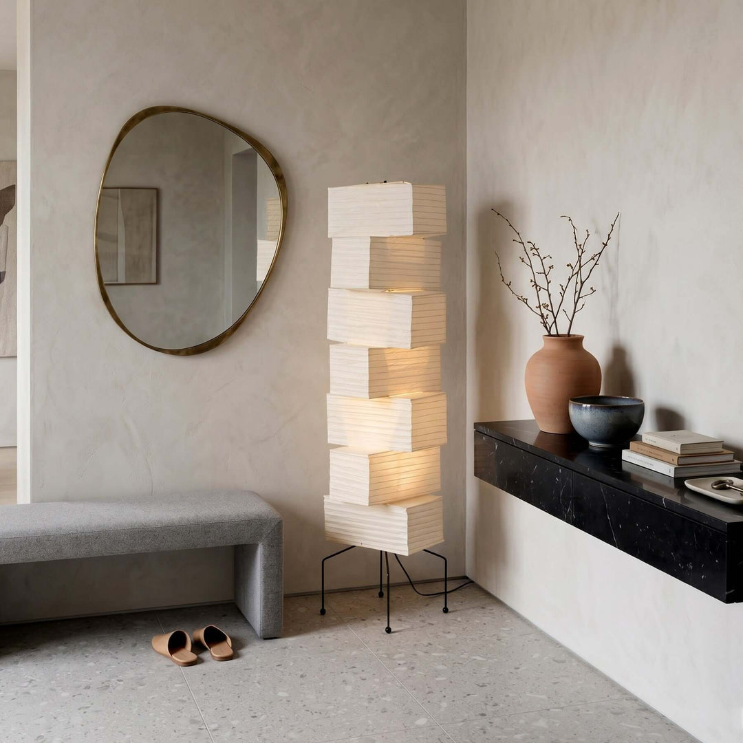 White rice paper floor lamp beside an organic mirror, upholstered bench and floating console in a minimalist entryway