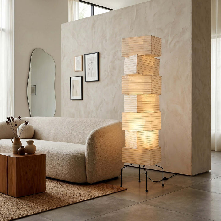 Akari rice paper living room floor lamp beside a curved cream sofa and sculptural wall mirror