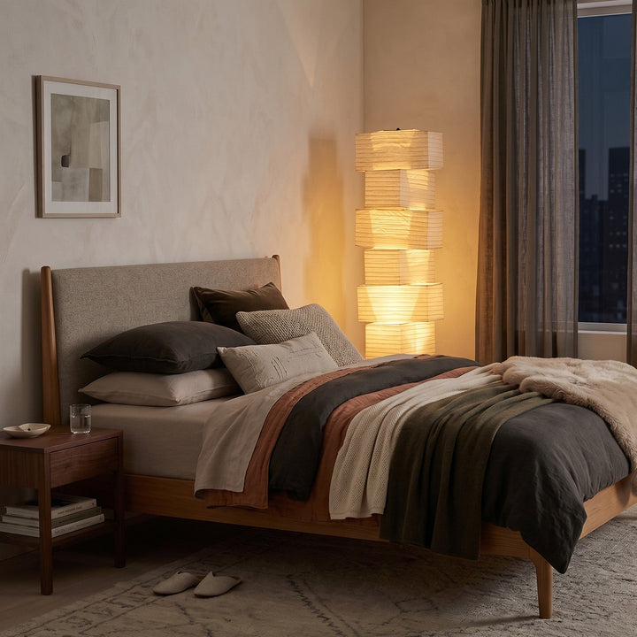 Akari UF4-L10 floor lamp casting warm diffused light beside an upholstered bed in a cozy bedroom