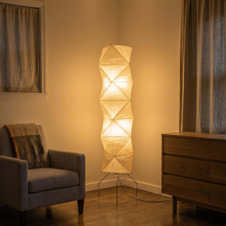 Glowing Akari UF4-L8 floor lamp between an armchair and wood cabinet in a cozy evening interior