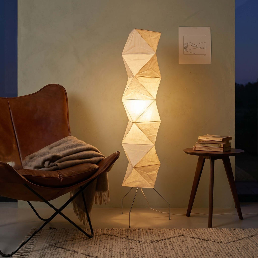 Glowing Akari UF4-L8 floor lamp beside a brown leather lounge chair and stacked books at night