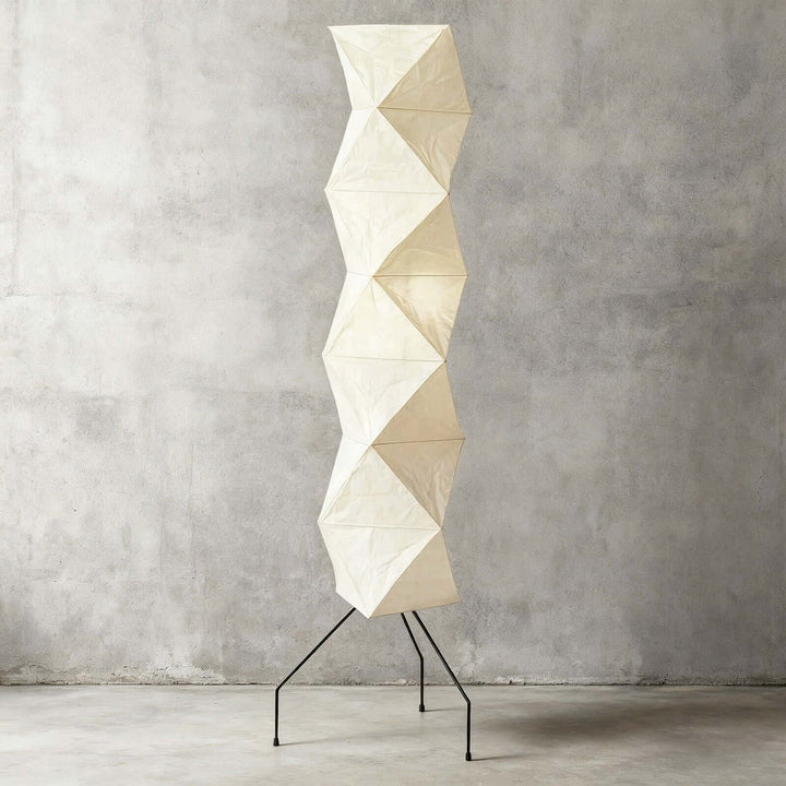 Illuminated Akari UF4-L8 floor lamp with a beige sculptural paper shade against a gray concrete wall