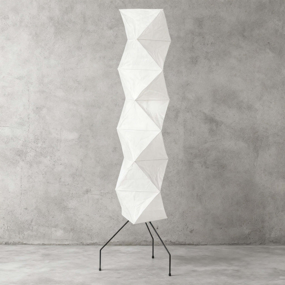 Unlit Akari UF4-L8 floor lamp with a white sculptural shade and black wire base against a concrete wall