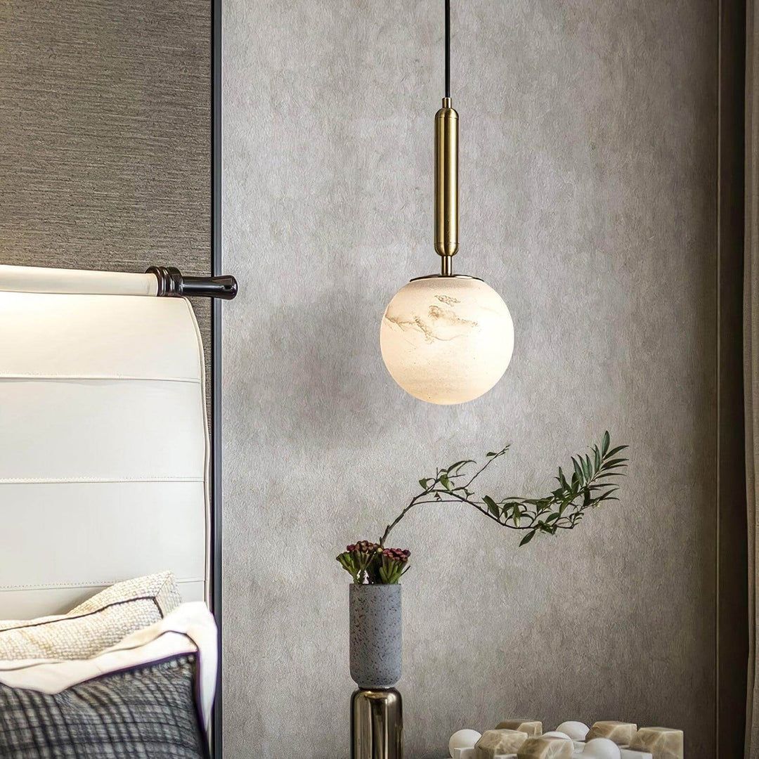 Close view of an illuminated alabaster globe pendant light beside a bed with brass hardware