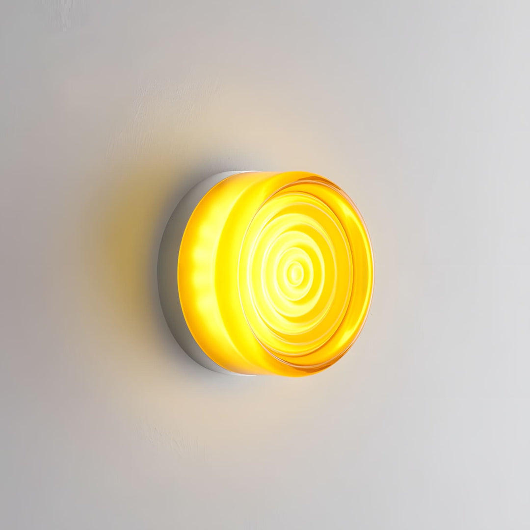 Amber glass wall sconce with concentric circular texture glowing on a gray wall.
