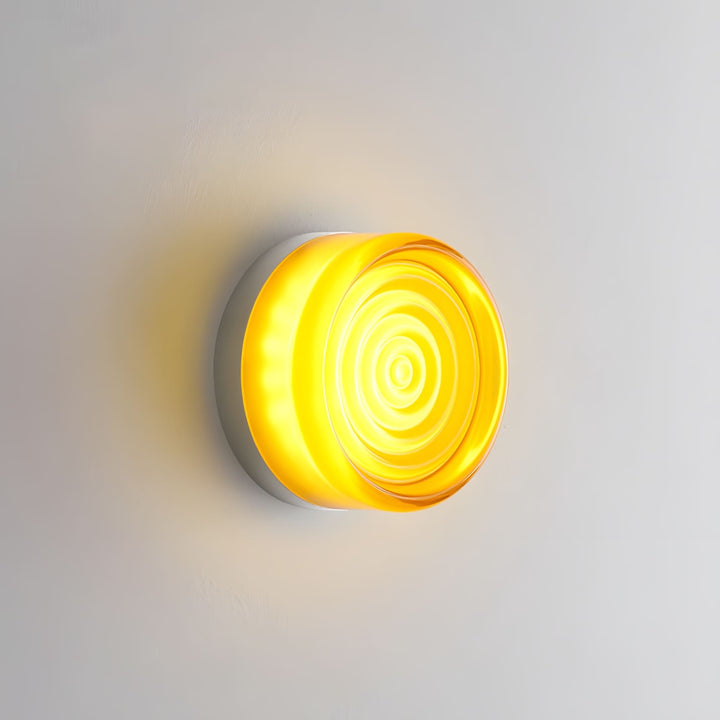 Amber glass wall sconce with concentric circular texture glowing on a gray wall.