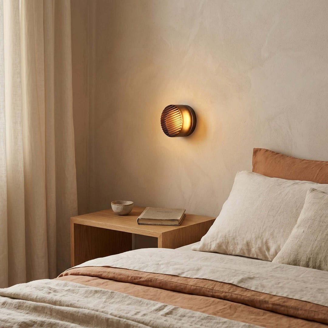 Amber Dimple wall sconce glowing beside a bed and curtain.