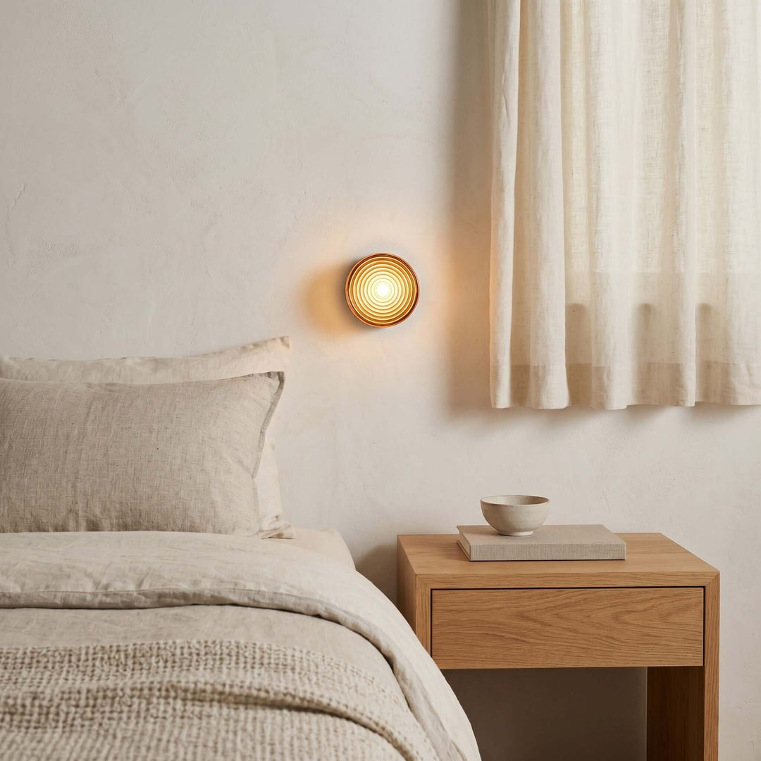 Amber Dimple wall sconce glowing beside a bed and wood nightstand.