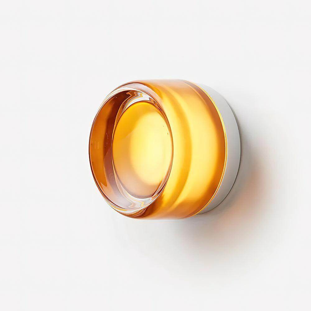 Close side view of an amber glass wall sconce with a clear raised lens.