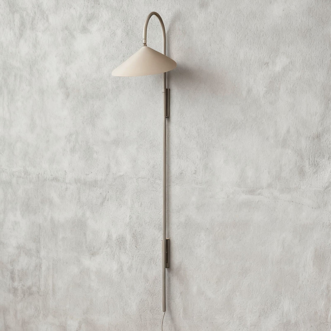 Long beige Arum plug-in wall sconce with a curved upper arm and extended metal stem on a plaster wall