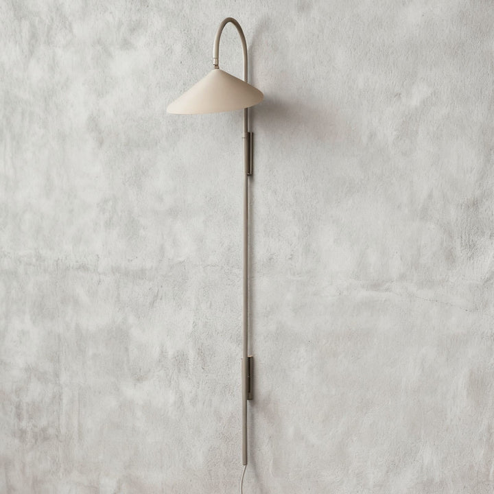 Long beige Arum plug-in wall sconce with a curved upper arm and extended metal stem on a plaster wall