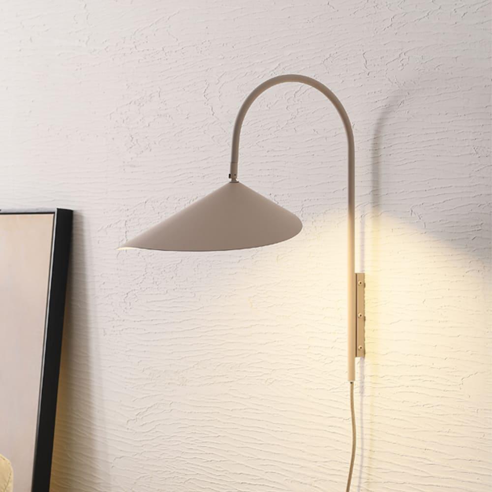 Beige Arum plug-in wall sconce with a curved arm and adjustable conical metal shade on a textured wall