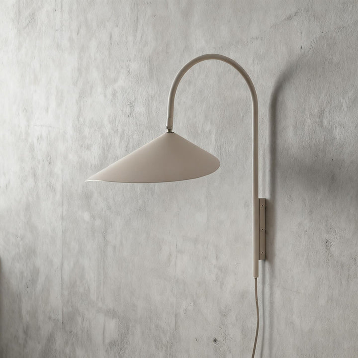 Short beige Arum plug-in wall sconce with a wide metal shade and visible power cord on a plaster wall