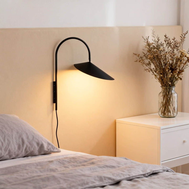 Black Arum bedroom wall sconce glowing beside a bed and white dresser with dried flowers