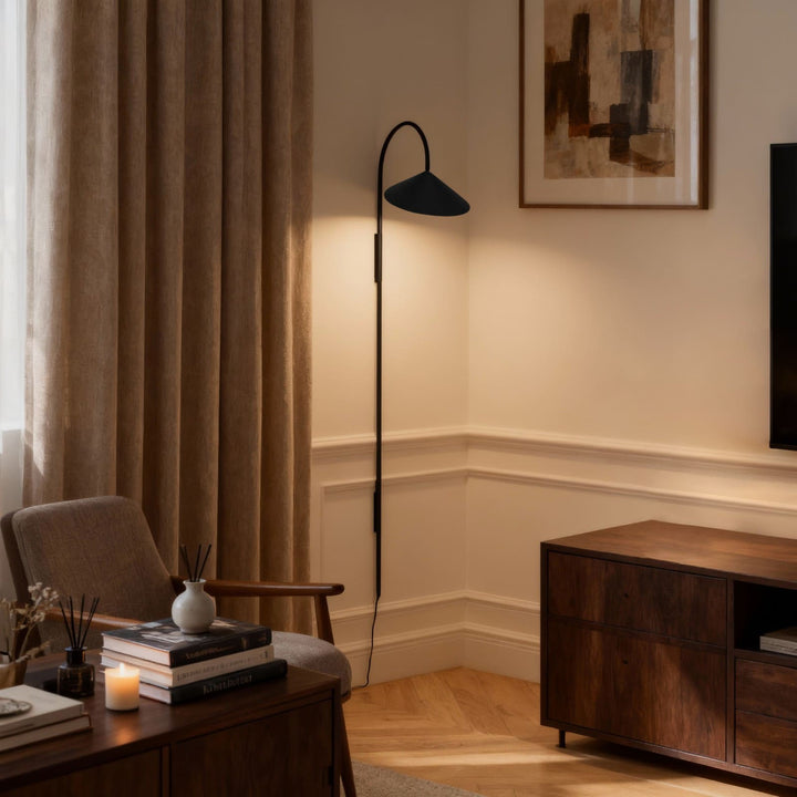 Long black Arum plug-in wall sconce lighting a living room corner with a chair and wood media console