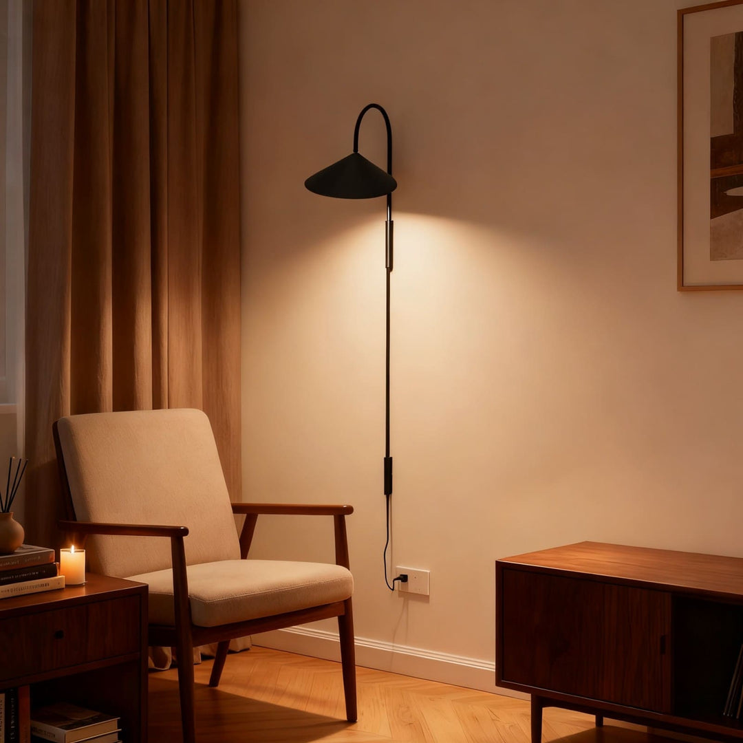 Long black Arum plug-in wall sconce beside an upholstered reading chair with its cord connected to an outlet