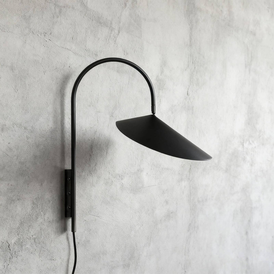Short black Arum plug-in wall sconce with a curved arm and conical shade on a gray plaster wall