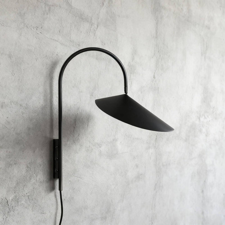 Short black Arum plug-in wall sconce with a curved arm and conical shade on a gray plaster wall