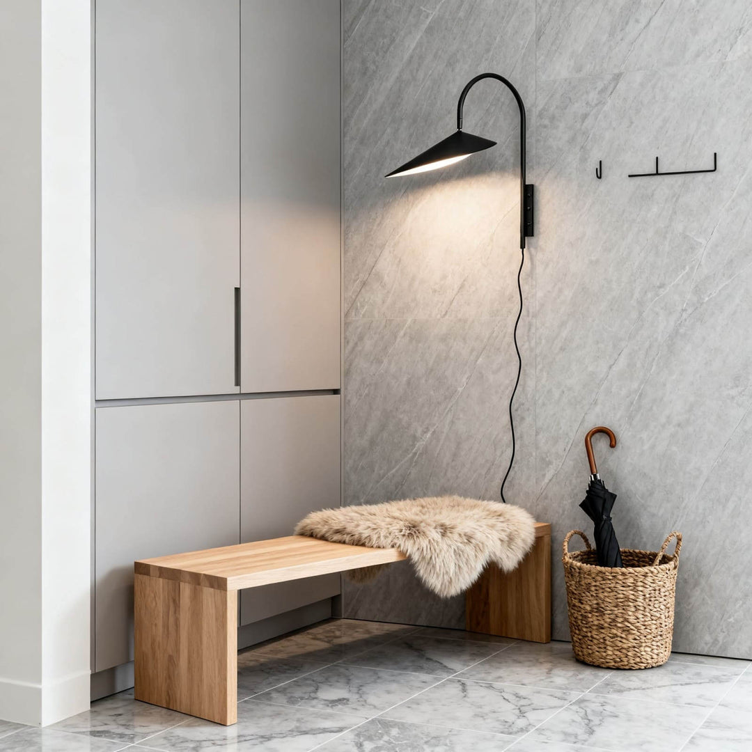 Black Arum plug-in wall sconce illuminating a wood bench against a gray marble entryway wall