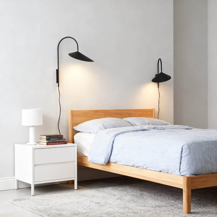 Pair of black Arum plug-in wall sconces in long and short sizes mounted beside a wood bed