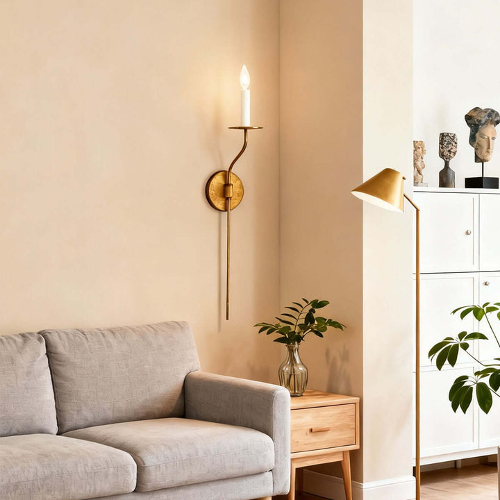 Tall aged brass candle wall sconce above a living room sofa in a warm minimalist interior