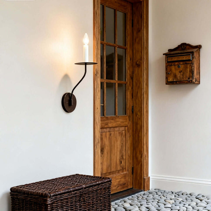Black single-light candle wall sconce illuminating a rustic entryway beside a wood door