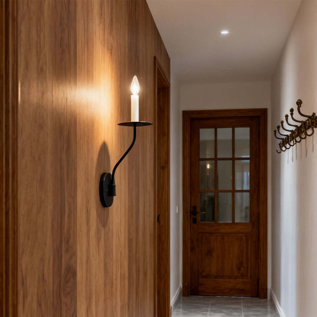 Black single-light candle wall sconce casting warm light across a wood-paneled hallway