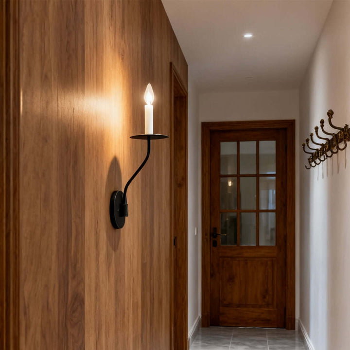 Black single-light candle wall sconce casting warm light across a wood-paneled hallway