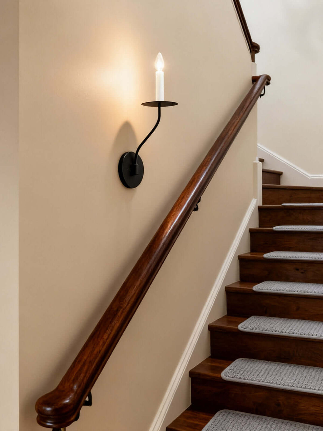 Black single-light candle wall sconce illuminating a traditional wood staircase and stairwell