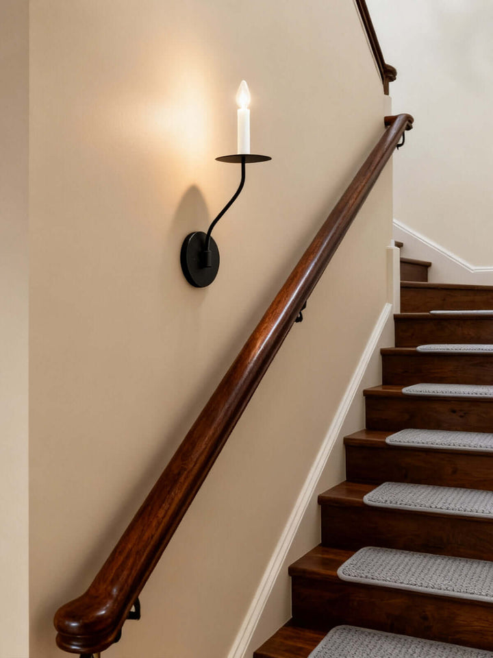 Black single-light candle wall sconce illuminating a traditional wood staircase and stairwell