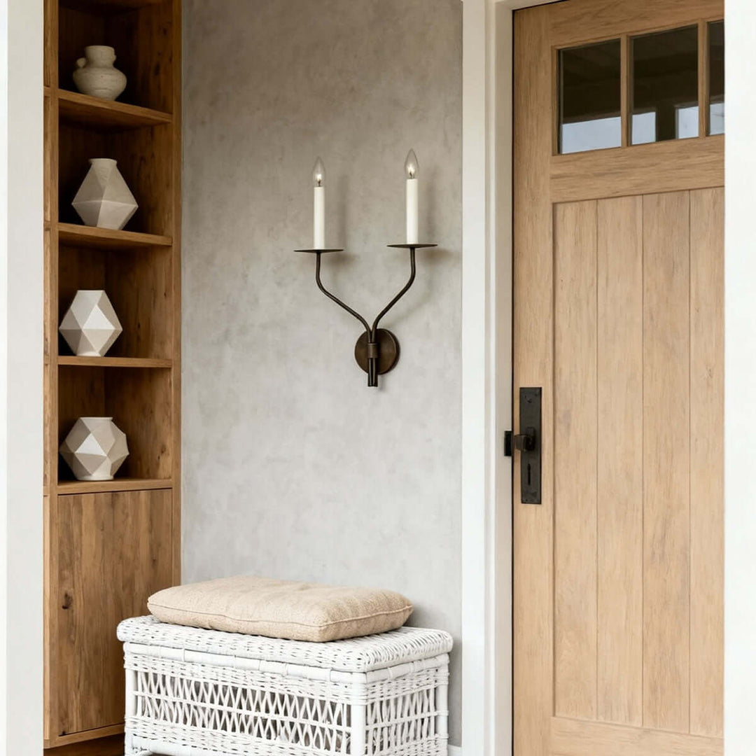 Two-light candle wall sconce with aged brass finish mounted beside a natural wood entry door