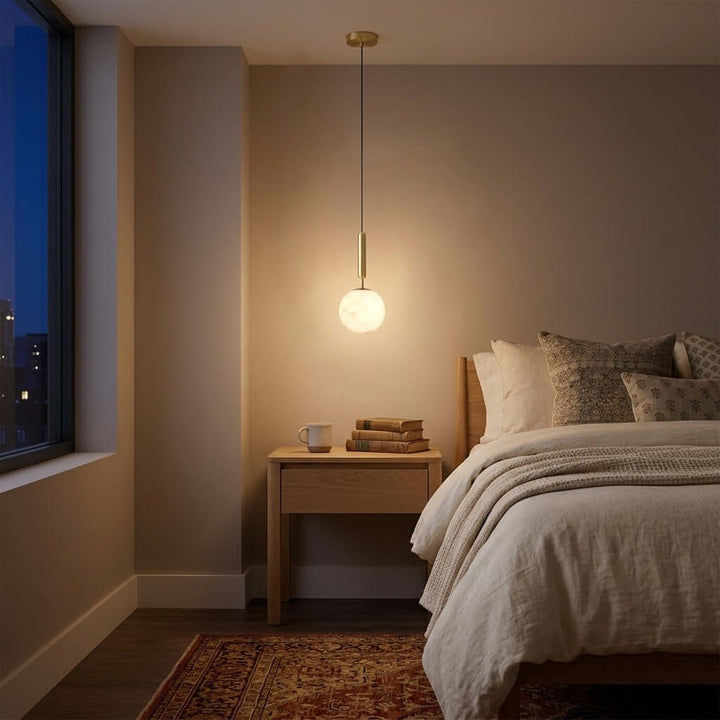 Small alabaster bedroom pendant light glowing beside a bed in a warm evening interior