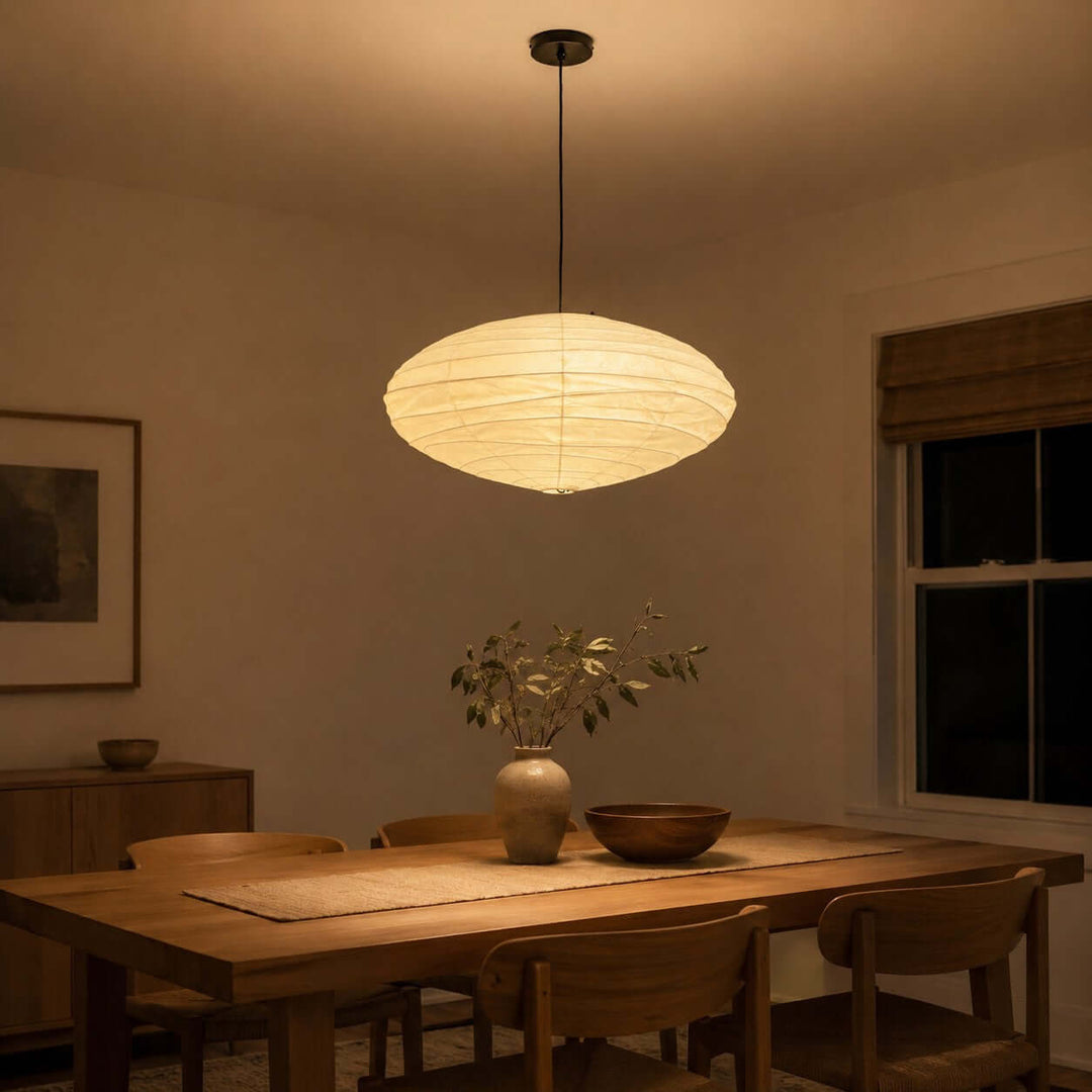 Black cord washi paper pendant light glowing above a dining table at night.
