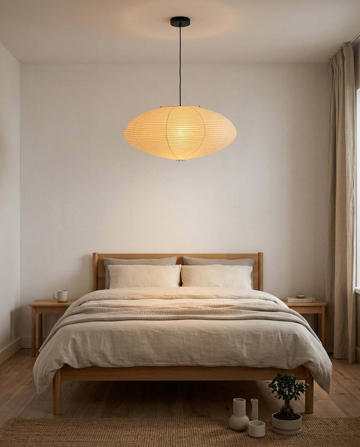 Black cord washi paper pendant light centered above a bed.
