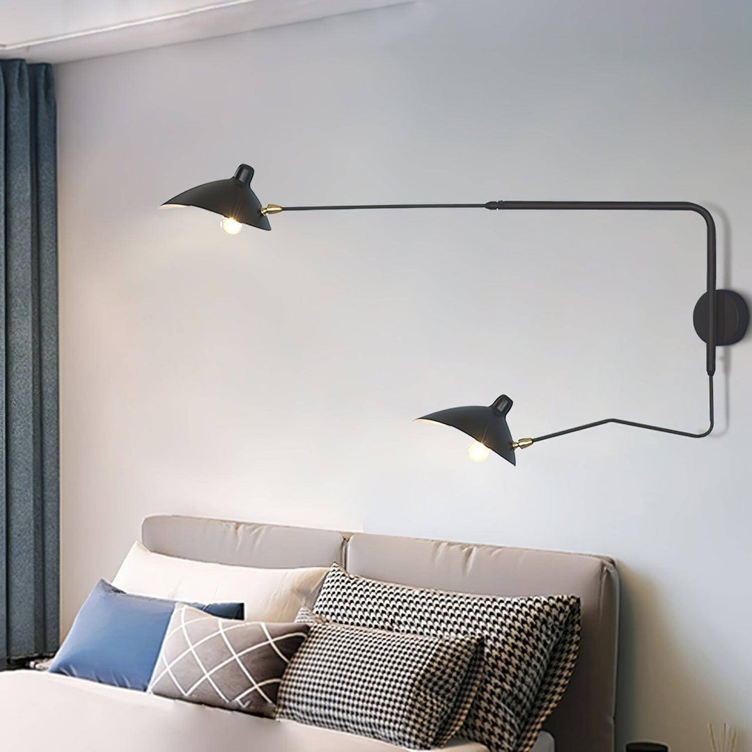 Black two-light swing arm wall sconce above an upholstered bed with patterned pillows