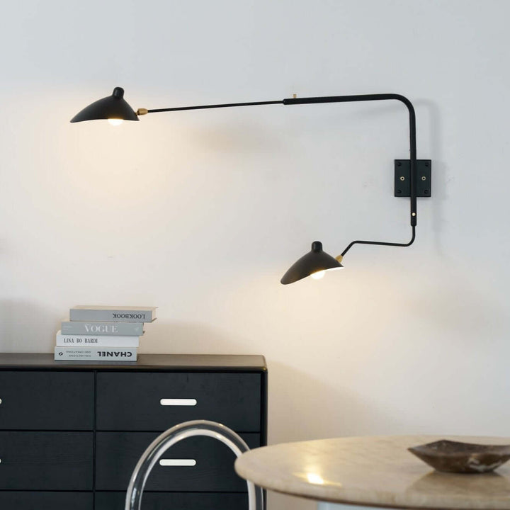 Black two-light swing arm wall sconce illuminating a modern dining area