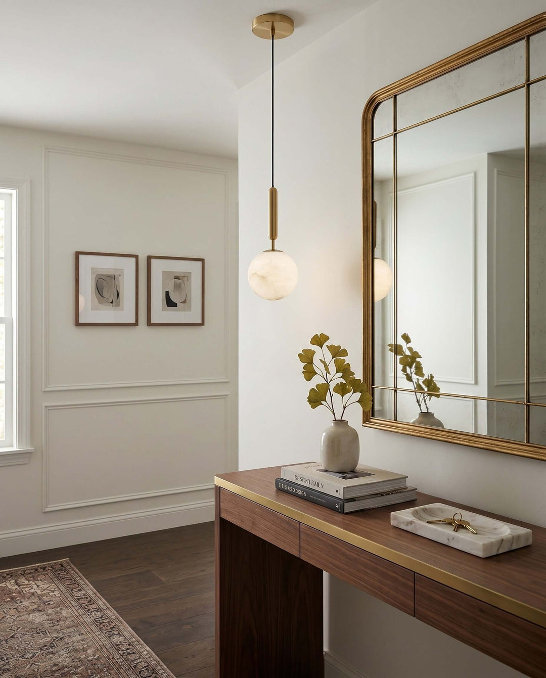 Brass and alabaster pendant light illuminating a wood console and mirror in a modern entryway