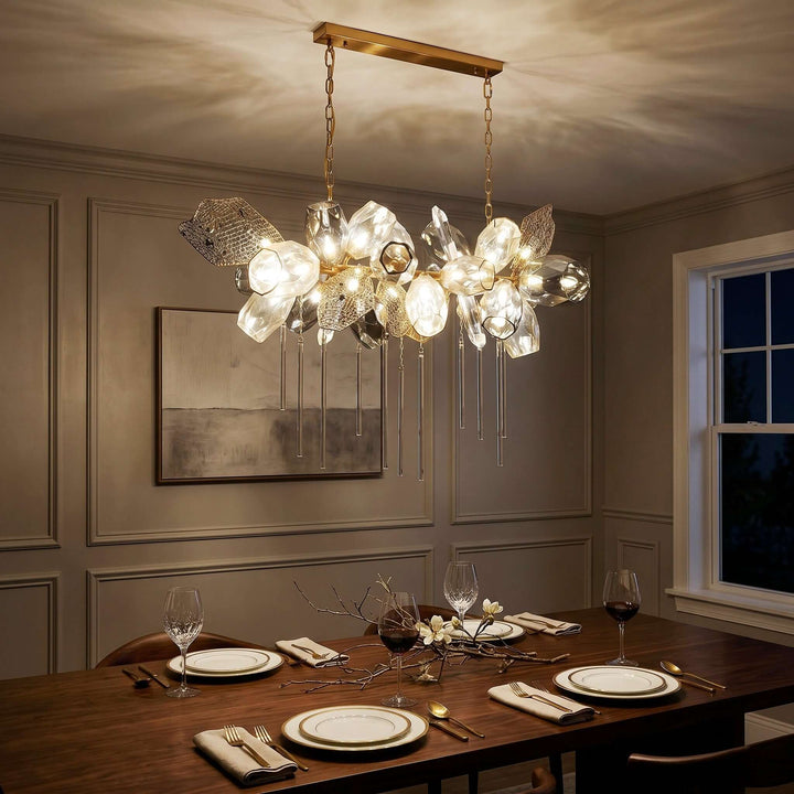 Horizontal Britannica dining area chandelier casting warm light above a set wood table at night.